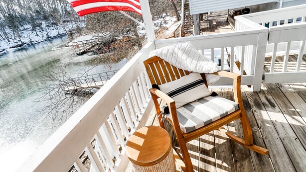 Une terrasse en bois avec un fauteuil à bascule et un panier en osier, donnant sur un paysage enneigé où flottent des drapeaux américains.