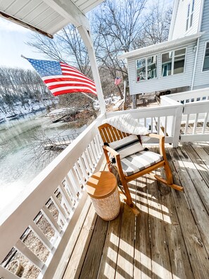 A wooden deck with a rocking chair and a wicker basket, overlooking a snowy landscape with American flags. - quiet & clean lakefront, private dock & HOT TUB (Linn Creek)