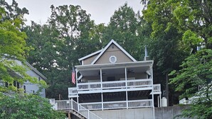 Une jetée en bois menant à un bâtiment doté d’un balcon, entouré d’arbres et bordé par une étendue d’eau.
