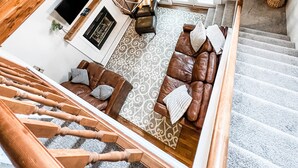 Un espace de vie moderne de style loft, doté d’un escalier, de murs en bois, d’un canapé en cuir marron et d’un luminaire au design géométrique.