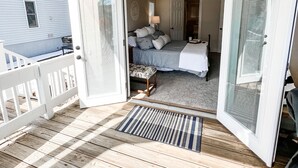 Une porte ouverte donnant sur une chambre à coucher, où l’on aperçoit un lit, une table de chevet et une lampe.