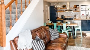 Un vaste espace de vie agrémenté d’un canapé en cuir marron, de fauteuils turquoise et d’un escalier en bois menant à l’étage supérieur.