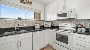 A modern kitchen with white cabinets, a black countertop, a microwave, an oven, and a sink. - Cocoa Beach Direct Oceanfront Condo - just a few steps to the beach! (Cocoa Beach)