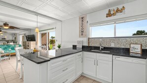 A modern kitchen with white cabinetry, a black countertop, and a window overlooking a garden. - Cocoa Beach Direct Oceanfront Condo - just a few steps to the beach! (Cocoa Beach)