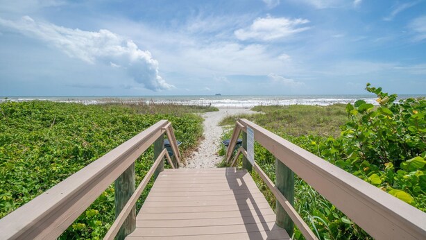 A wooden boardwalk leading to a beach with a clear view of the ocean and sky. - Cocoa Beach Direct Oceanfront Condo - just a few steps to the beach! (Cocoa Beach)