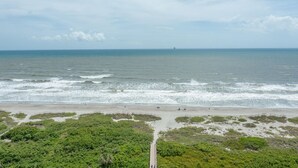A coastal beach with a pathway leading to the water, surrounded by dense greenery. - Cocoa Beach Direct Oceanfront Condo - just a few steps to the beach! (Cocoa Beach)