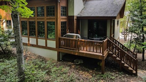 Une cabane dotée de grandes fenêtres, d’une terrasse et d’un escalier menant à un espace abrité.