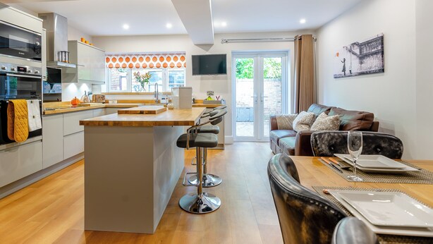 A modern kitchen with a central island, a dining area with a table set for two, and a living area with a sofa and a TV.