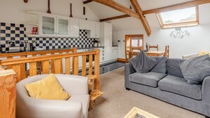 A cozy living room with a grey sofa, a white armchair, and a wooden bench. A kitchen with white cabinets and a checkered backsplash is visible in the background. - Robin’s Nest - UK36208 (Capel Seion, near Aberystwyth)