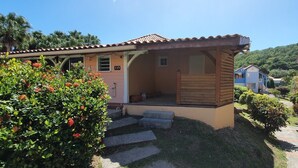 A small wooden cabin with a tiled roof, surrounded by lush greenery and a clear sky. - Maisonette with terrace, 2 air-conditioned bedrooms  (Saint Anne)