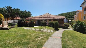 A residential area with a house featuring a tiled roof, a stone pathway leading to the entrance, and a small bridge over a water feature. - Maisonette with terrace, 2 air-conditioned bedrooms  (Saint Anne)