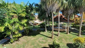 A well-maintained garden with palm trees, a gazebo, and a pathway leading to a building with a tiled roof. - Maisonette with terrace, 2 air-conditioned bedrooms  (Saint Anne)
