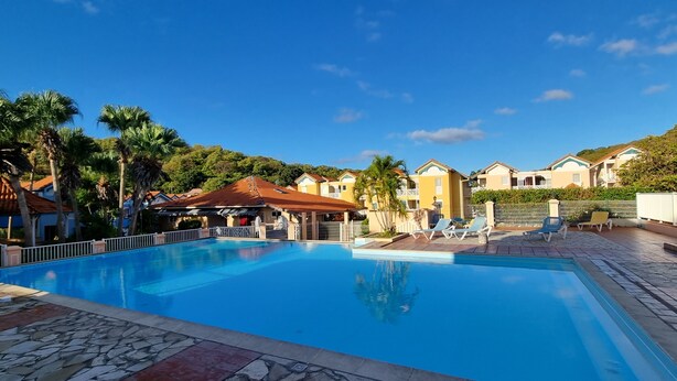 A swimming pool with lounge chairs, a covered area, and a backdrop of houses and palm trees. - Maisonette with terrace, 2 air-conditioned bedrooms  (Saint Anne)