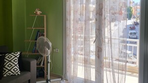Una sala de estar con pared verde, un sofá, un ventilador, una mesa con bebidas y una ventana con cortina.