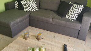 Una sala de estar con un sofá seccional gris, cojines estampados, una mesa de centro de madera con frascos y un control remoto, y una pared verde con un adorno sobre el sofá.