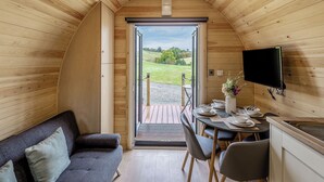 Un interior de cabaña acogedor con techo de madera, un sofá, una mesa de comedor con sillas y un televisor montado en la pared.