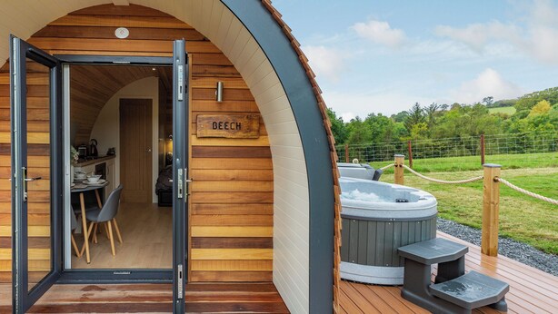 Una cabaña de madera acogedora con un cartel que dice "BEECH" y un jacuzzi en la terraza.