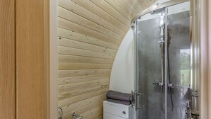 Un baño pequeño con pared de madera, cabina de ducha de vidrio, inodoro y lavamanos.