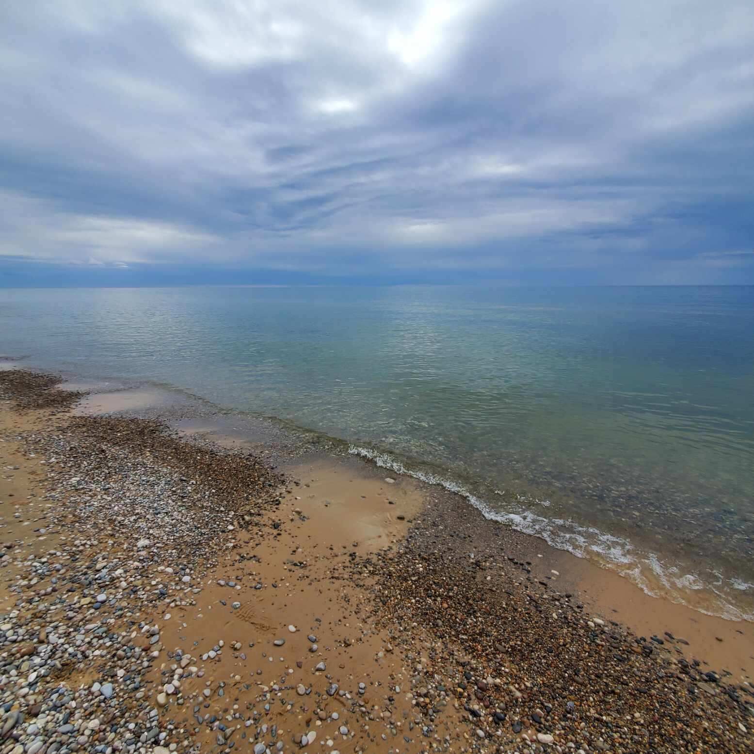 A beach with pebbles and sand, and the ocean in the background.