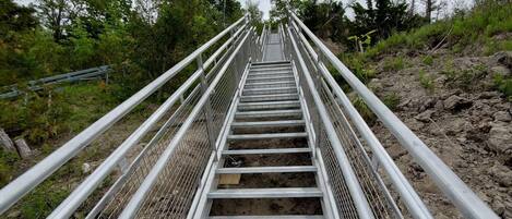 Un escalier métallique avec des rampes menant vers le haut, entouré de verdure et d’arbres.