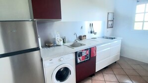 A compact kitchen with a built-in washing machine, a stainless steel refrigerator, and a small sink. - Spacious apartment on the top floor of a villa with a large terrace and a magnificent ocean view (Sainte-Luce)