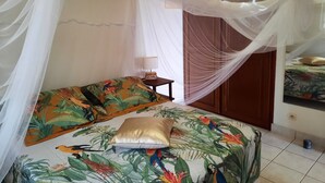 Een slaapkamer met een hemelbed, een nachtkastje met lamp, en een deur die naar een andere kamer leidt.