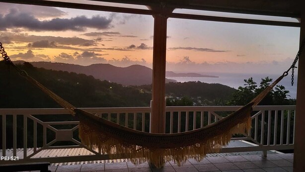 Een hangmat op een balkon met uitzicht op bergen en een zonsondergang.