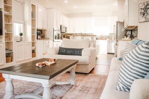 A spacious living room with a coffee table, a sofa with a pillow, and a kitchen in the background.