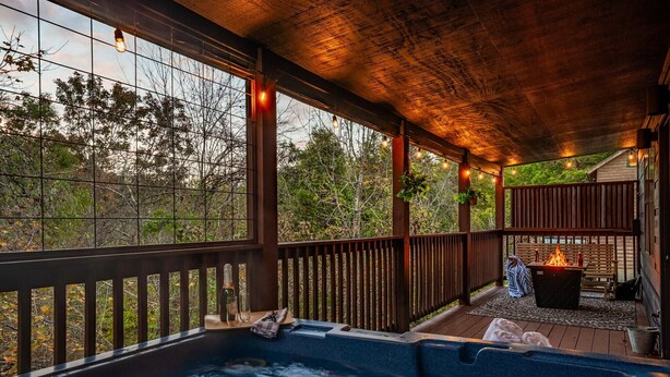 A hot tub area with a wooden deck, a fire pit, and a view of trees.
