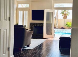 A living room with a fireplace, a TV, and a pool area visible through an open door. - Las Vegas Pool Home Near Strip /Airport Holiday Dates Open & Discount Available
 (Las Vegas)