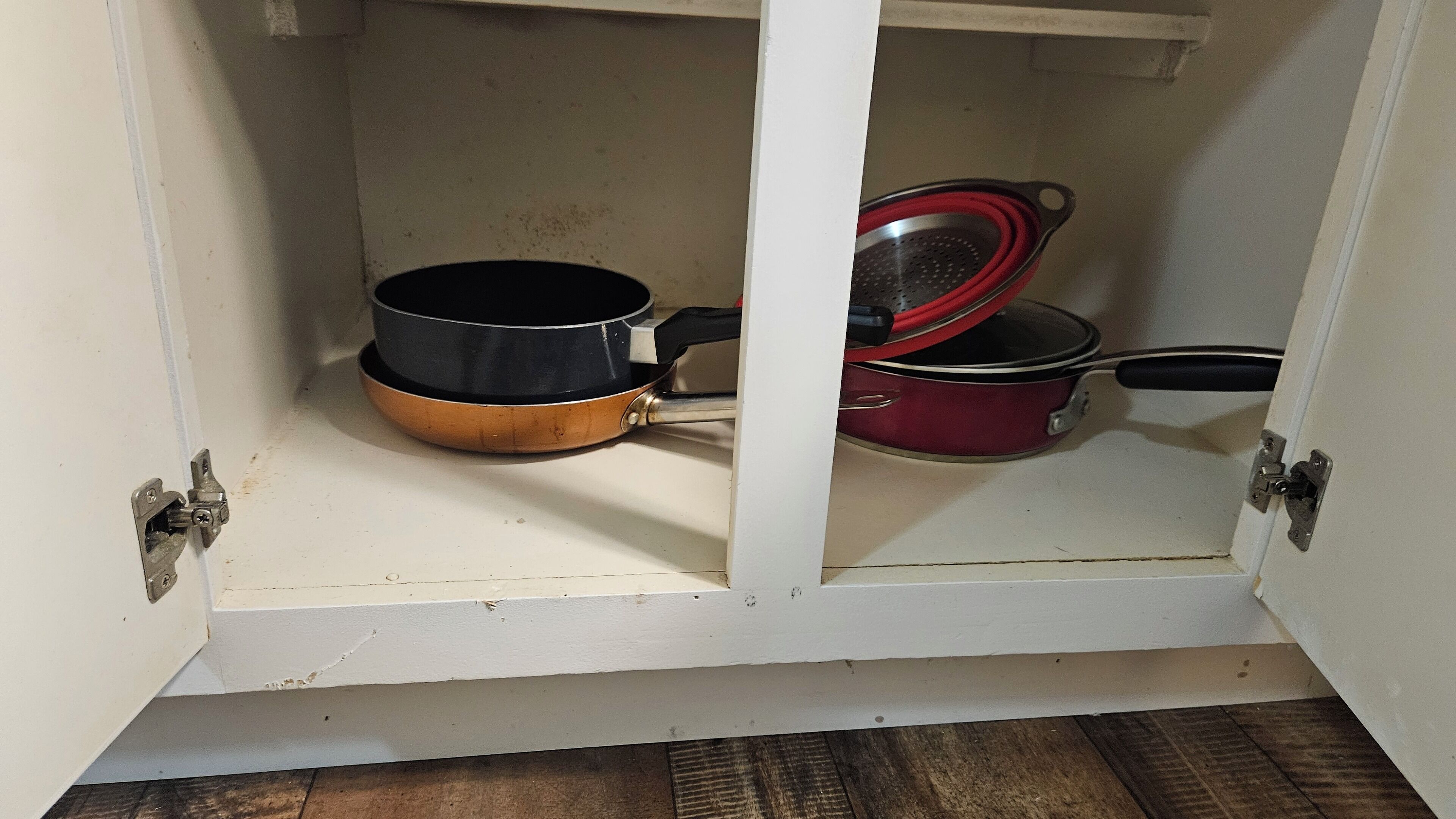 Un armario de cocina con dos ollas, una negra y otra roja, y un colador de metal.