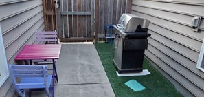 A patio with a grill, a red table, and a blue chair.