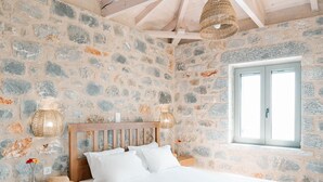 Une chambre avec un mur en pierre, des poutres en bois au plafond, un lit, des tables de chevet et une fenêtre.