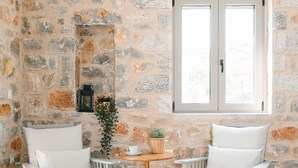 Une pièce avec deux fauteuils blancs, une petite table en bois et un mur en pierre.