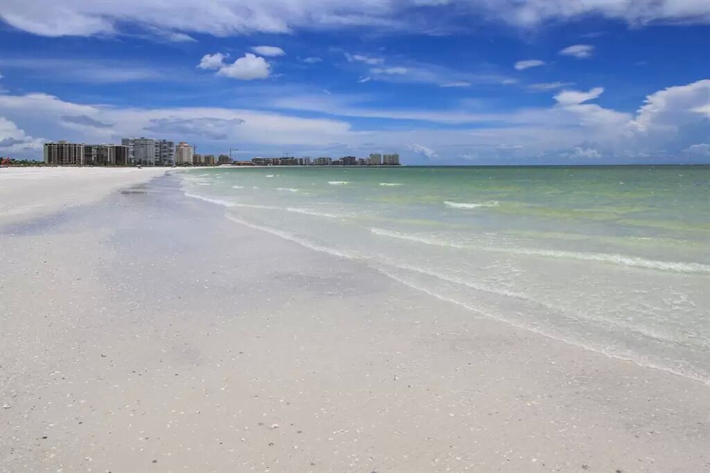 Une plage bordée d’une eau turquoise et limpide, avec une vue lointaine sur les gratte-ciel d’une ville.