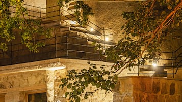 A stone building with a staircase leading to an upper level, surrounded by greenery.
