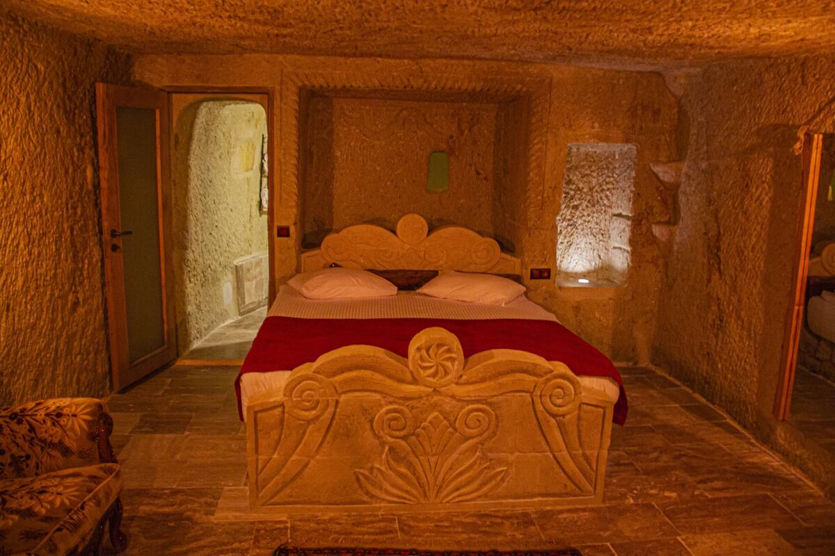 Dormitorio con paredes de piedra, una cama, una silla y una puerta que da al exterior.