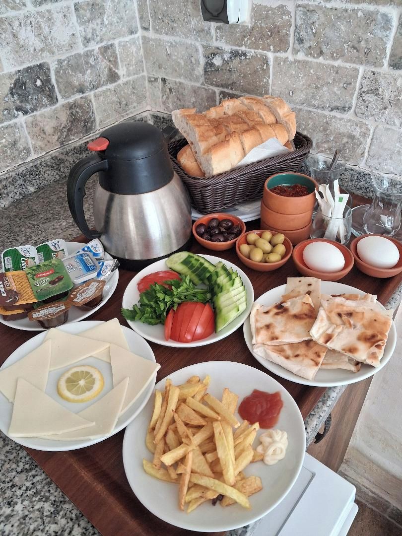 A breakfast table with bread, eggs, tomatoes, cucumbers, cheese, olives, and a coffee pot.