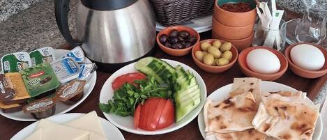 A breakfast table with bread, eggs, tomatoes, cucumbers, cheese, olives, and a coffee pot.