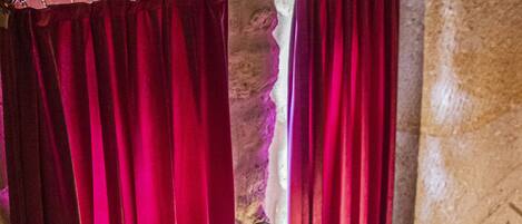 Una habitación con pared de piedra, una silla de madera y una cortina roja.