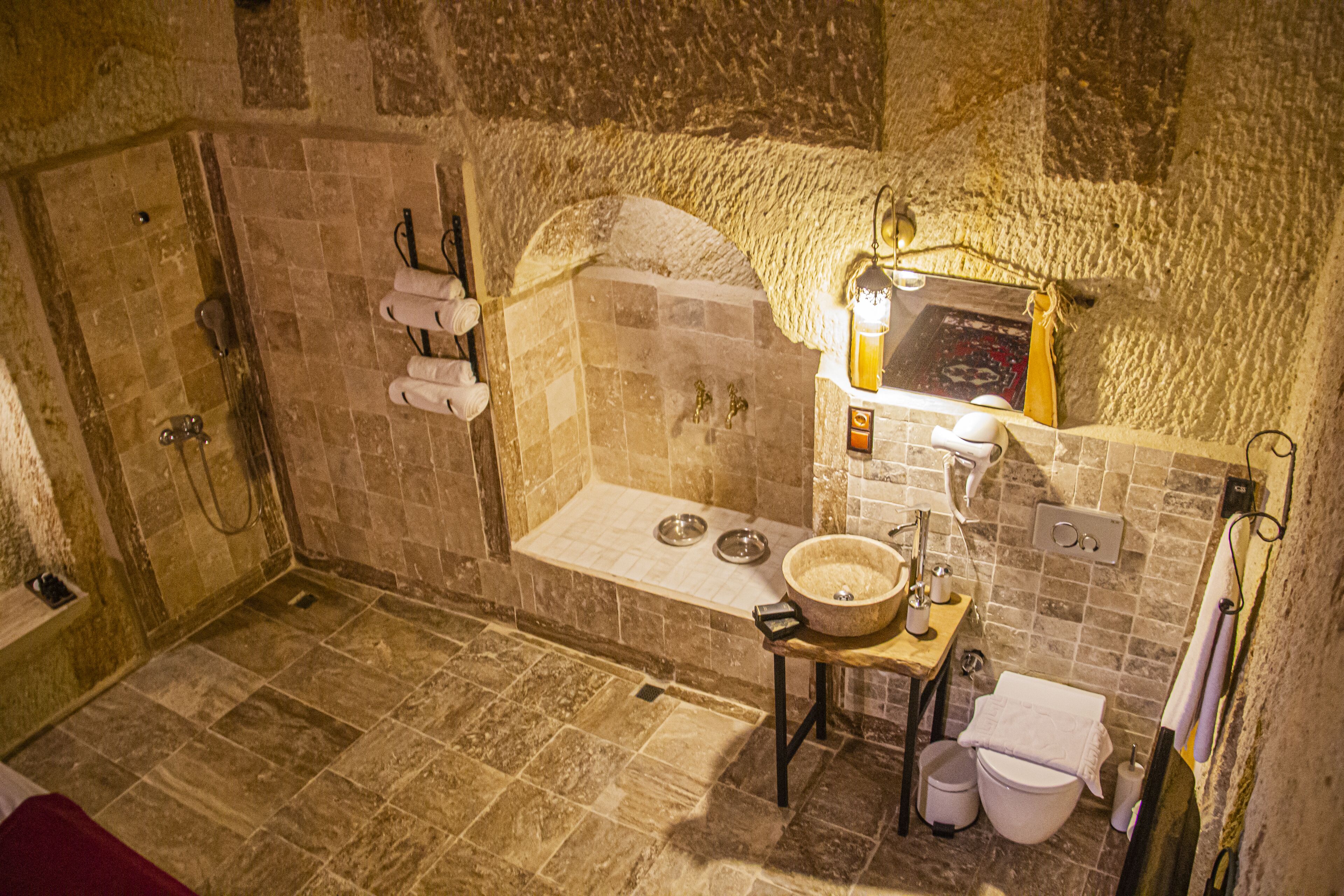Une salle de bain aux murs en pierre, équipée d’une baignoire, d’un lavabo et de toilettes.