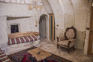 Una habitación con pared de piedra, un banco de madera con cojín estampado, una mesa de centro de madera y una alfombra con diseño.