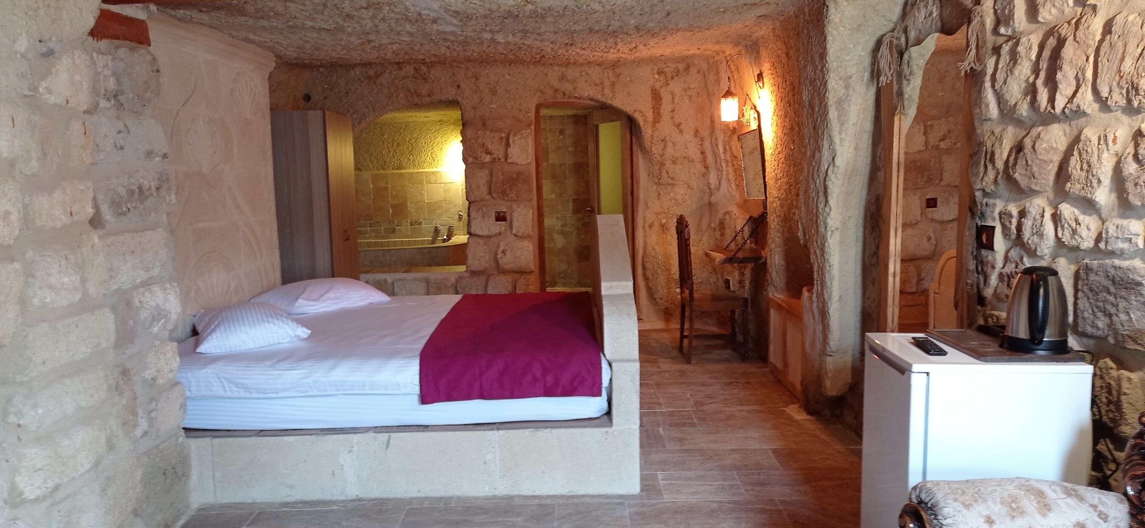 Un dormitorio con paredes de piedra, una cama, una mesita y un hervidor.
