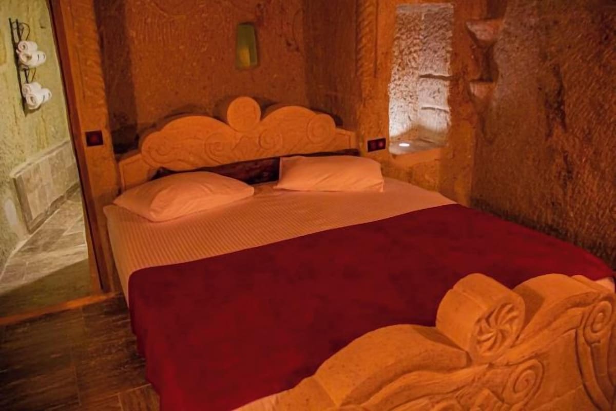 A room with a bed, a red blanket, and a stone wall.