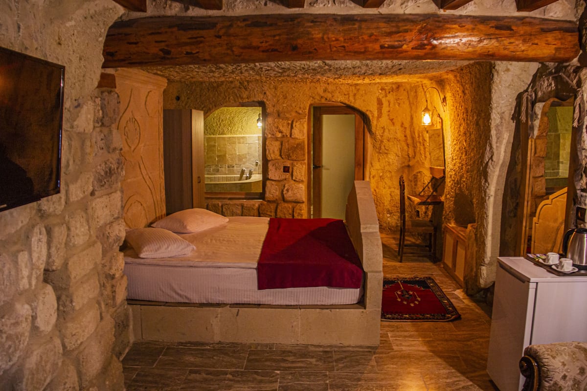 Un dormitorio con paredes de piedra, una cama, techo de madera y un pequeño escritorio con una taza y un platillo.