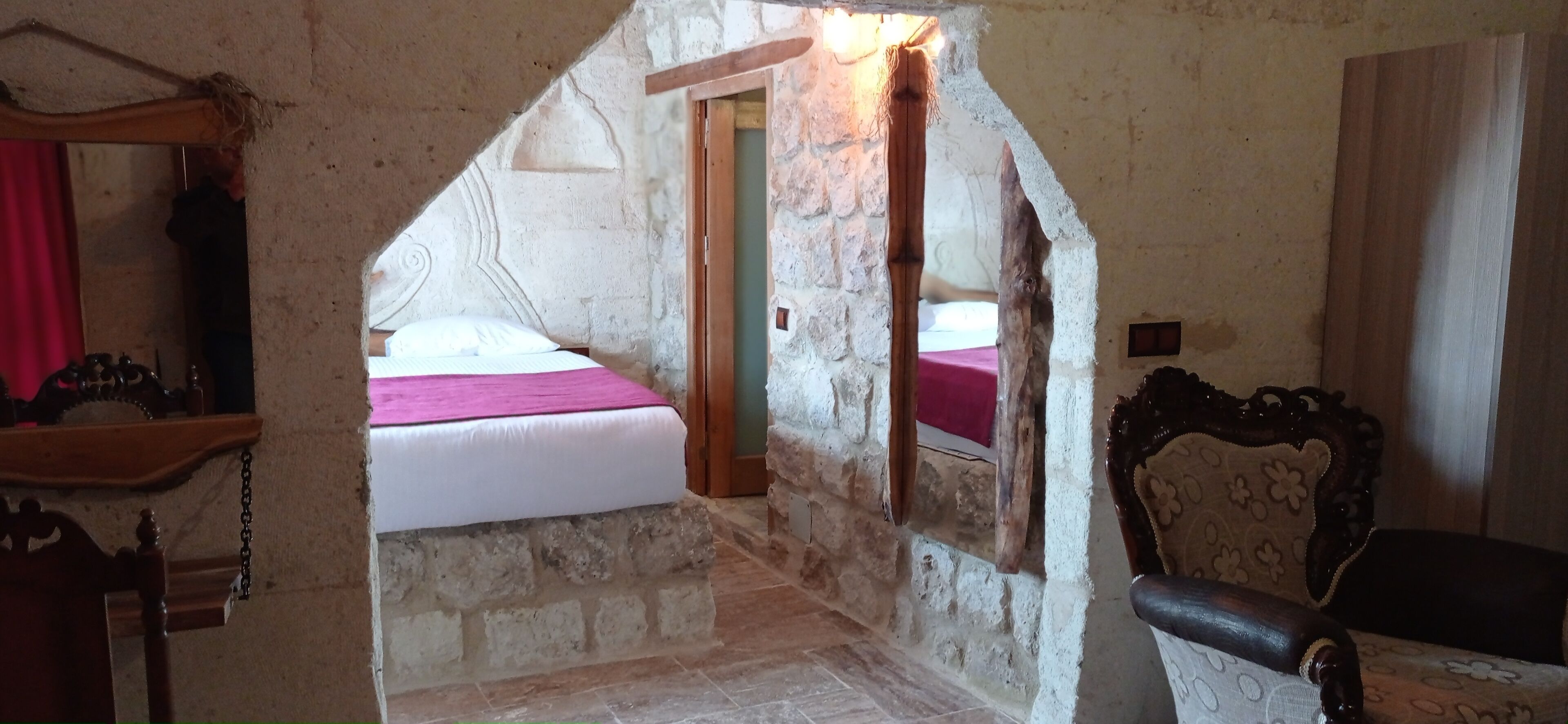 A narrow stone-walled corridor leading to a bedroom with a bed and a wooden chair.