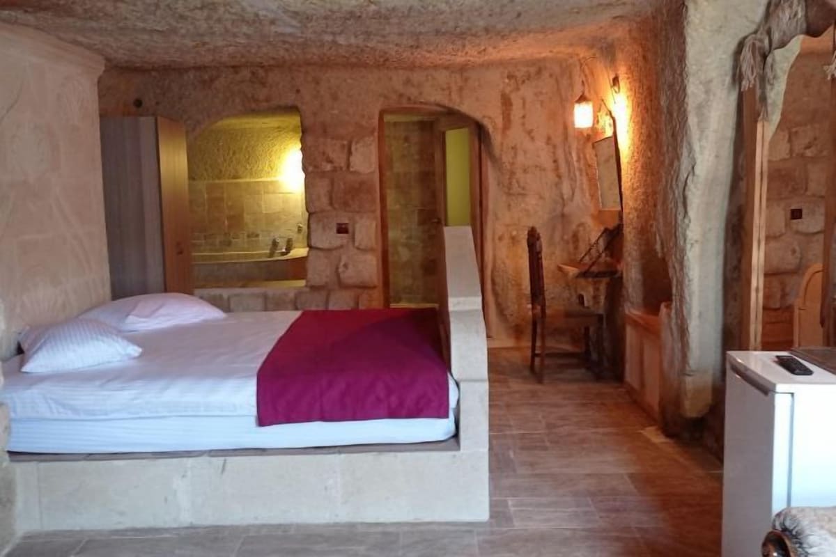 A stone-walled bedroom with a bed, a wooden chair, and a small table.