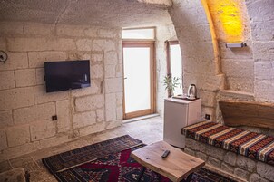 Una sala de estar acogedora con un televisor de pantalla plana montado en una pared de piedra, una mesa de centro de madera, un tapete estampado y un banco con cojines.