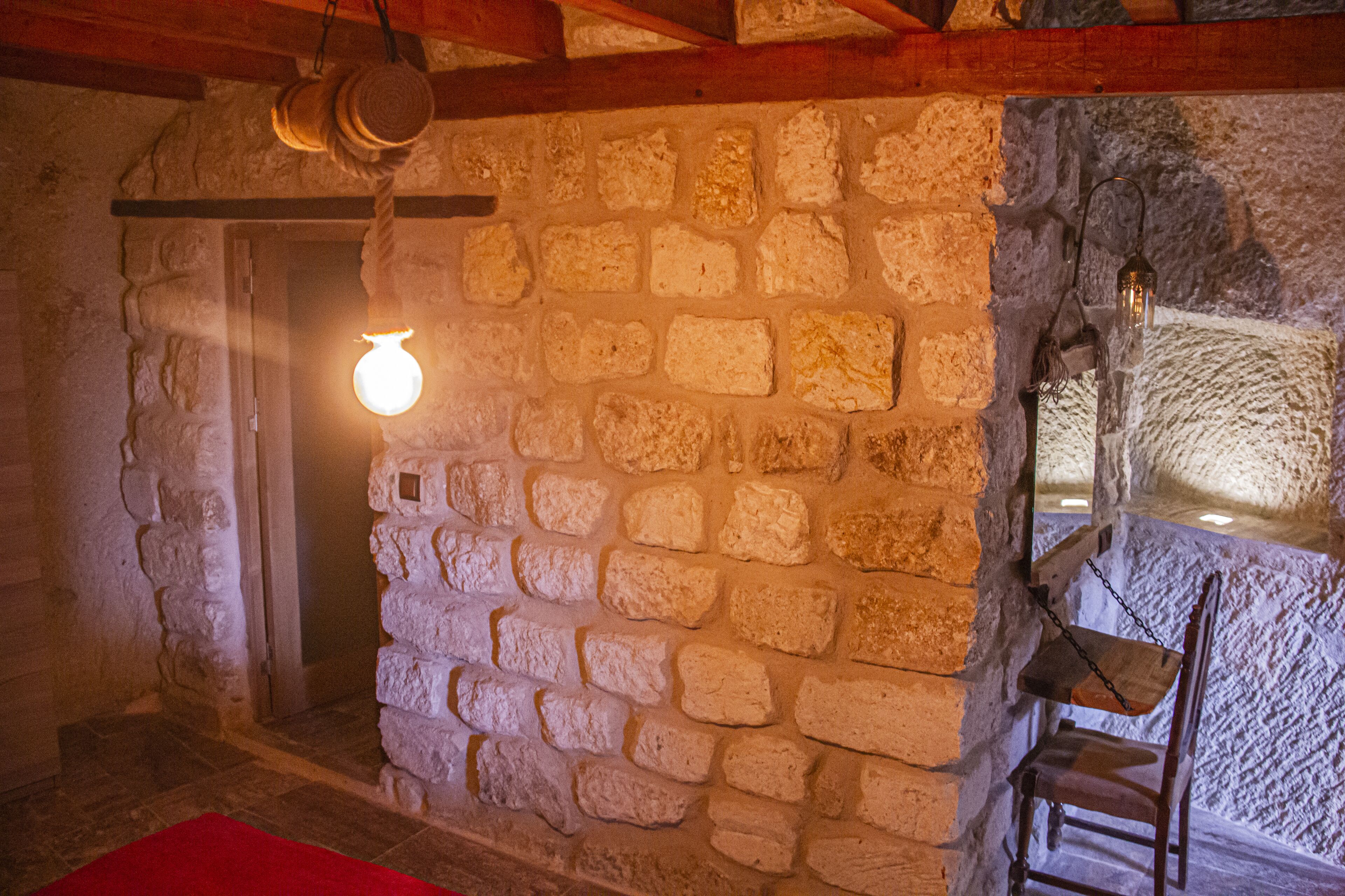 A rustic stone wall with a wooden chair and a hanging light fixture.