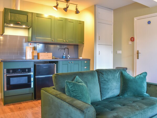 A compact kitchen with green cabinets, a built-in oven, and a refrigerator.